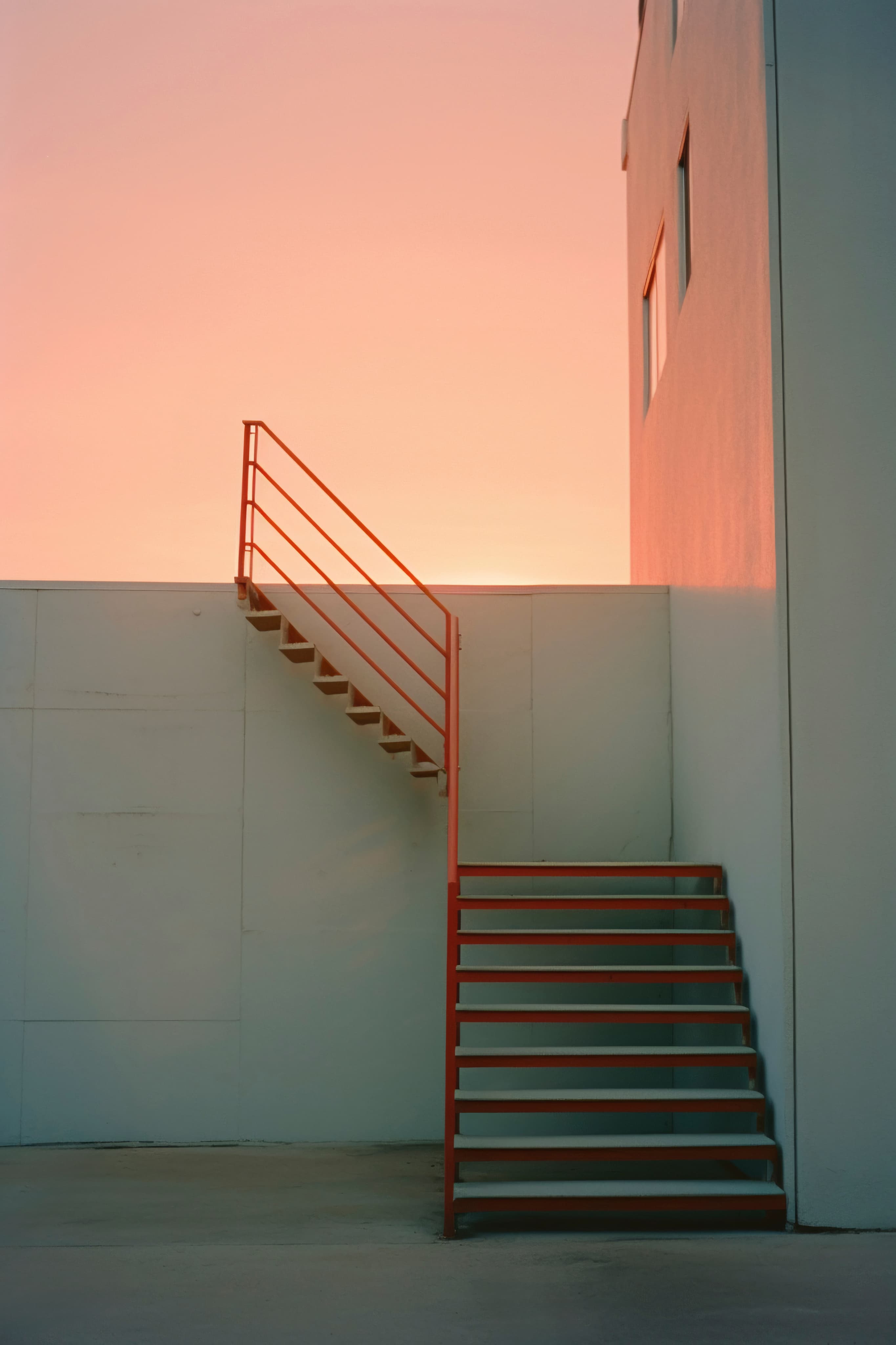 Red staircase against a pale concrete wall at sunset